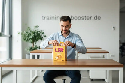 Mann öffnet Box mit Vanille-Waffeln von F*King Delicious im Büro, ideal als Sportnahrung oder Booster