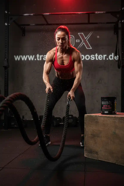 Frau trainiert mit Battle Ropes im Fitnessstudio – Booster & Sportnahrung für maximale Leistung