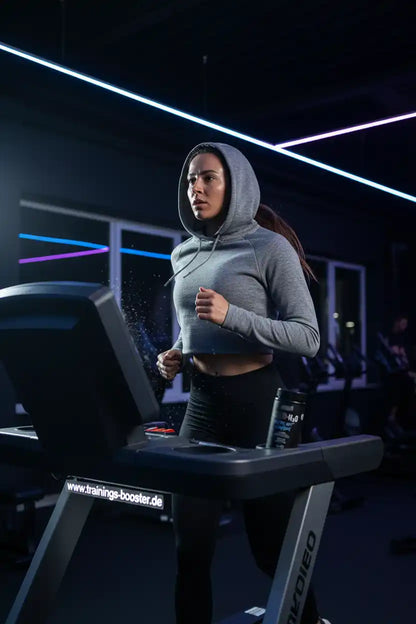 Frau trainiert auf Laufband im Fitnessstudio mit Sportnahrung und Booster