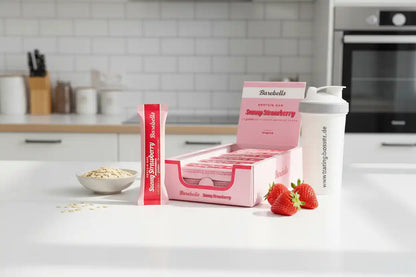 Barebells Protein Riegel Sunny Strawberry mit Shaker und frischen Erdbeeren in moderner Küche