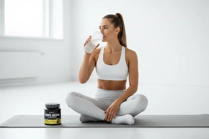 Frau trinkt Proteinshake neben 100% BCAA-Dose auf Yogamatte, Fitness und Sportnahrung