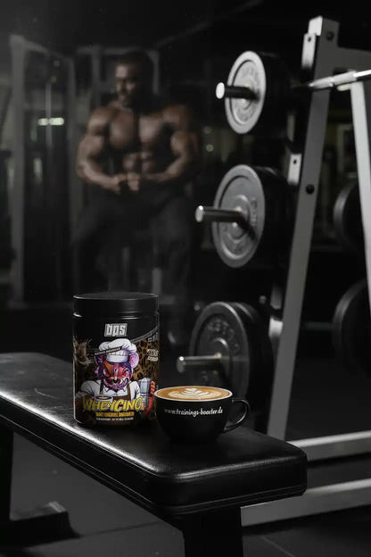 BPS Pharma WheyChino Proteindose neben einer Tasse Kaffee im Fitnessstudio