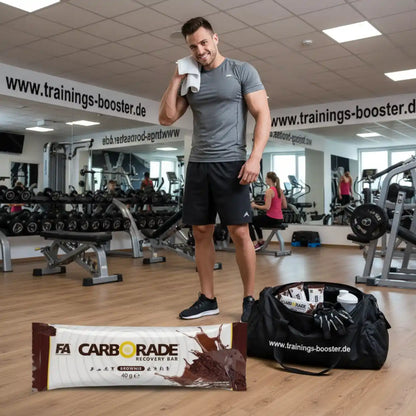 FA Nutrition Carborade Recovery Bar Brownie vor einem muskulösen Mann im Fitnessstudio