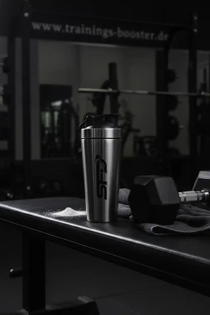 Edelstahl-Shaker mit SFB-Logo auf Trainingsbank, neben Hantel und Pulver, ideal für Sportnahrung und Booster